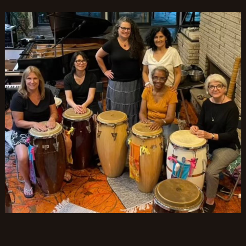 Six women in a half circle with drums in front of them