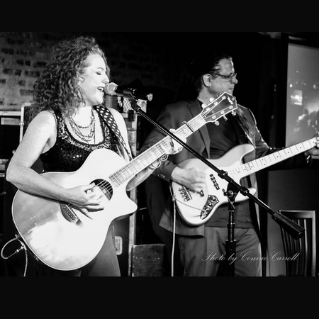 Two people standing at microphones, playing guitars